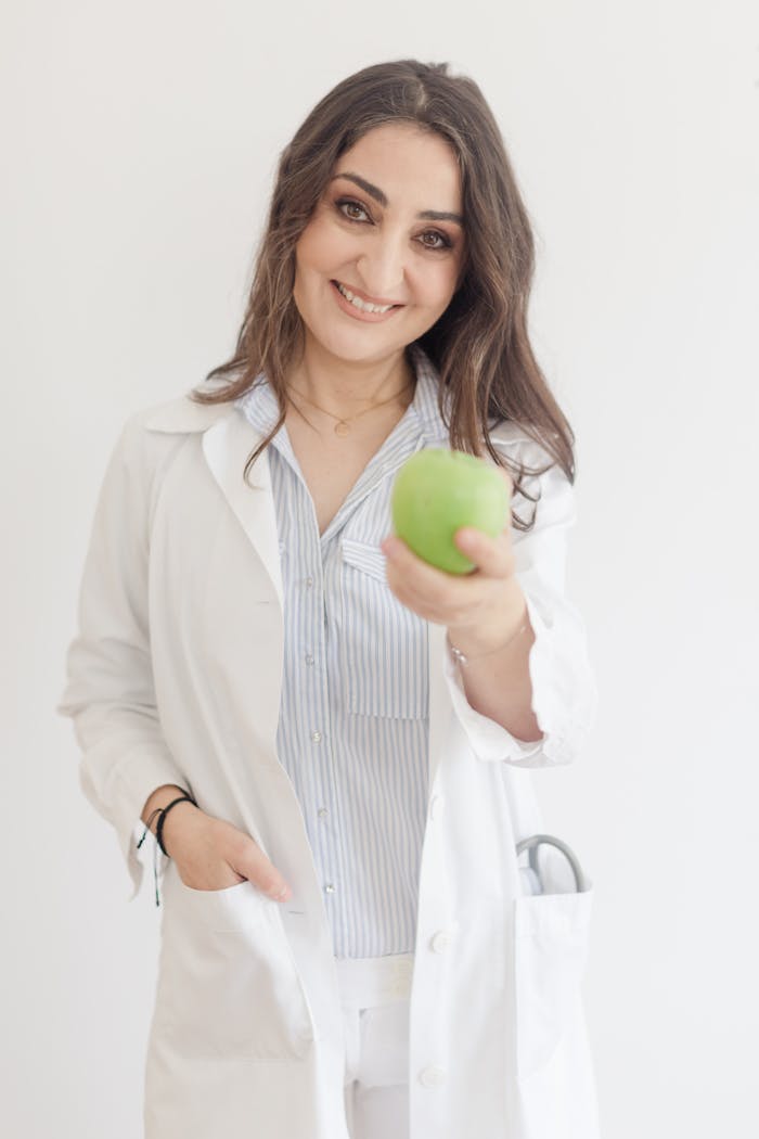 Smiling doctor in a medical gown holding a green apple, promoting health and wellness.
